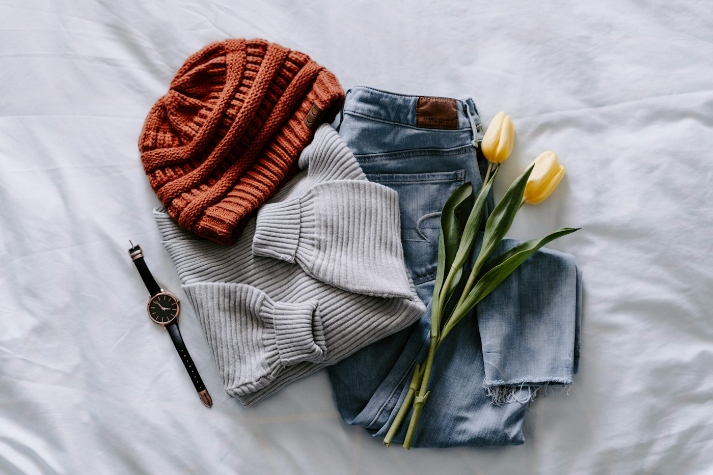 Un bonnet, un jean et un haut gris disposés à plat sur un drap blanc